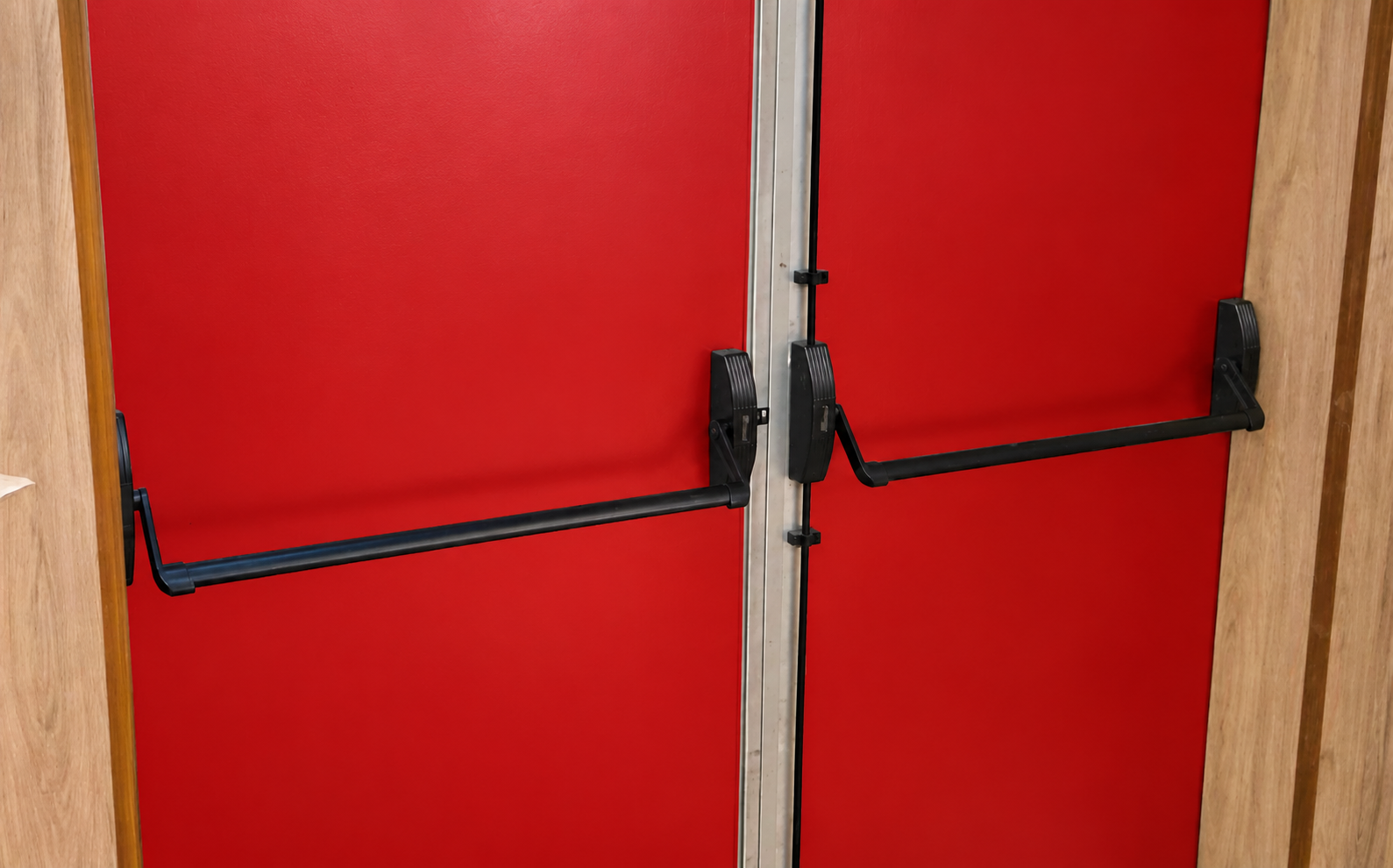 Barras antipânico pretas em porta de duas folhas com acabamento vermelho.