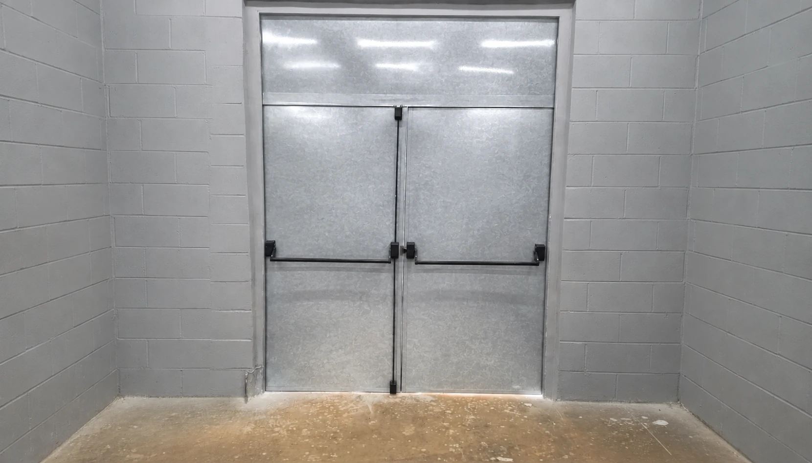 Porta de duas folhas com acabamento com aspecto metálico, painel superior e barras antipânico.