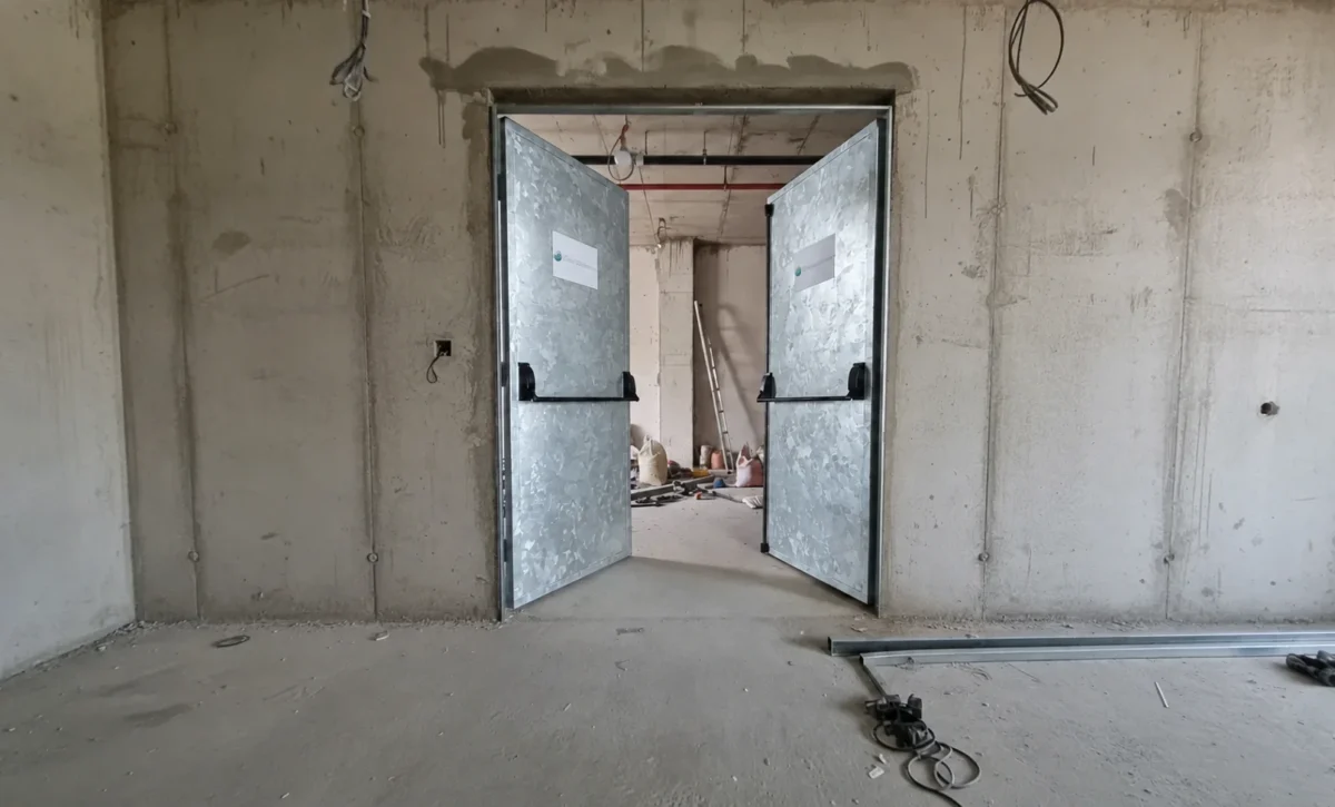 Porta de duas folhas abertas com acabamento com aspecto metálico e barras antipânico.