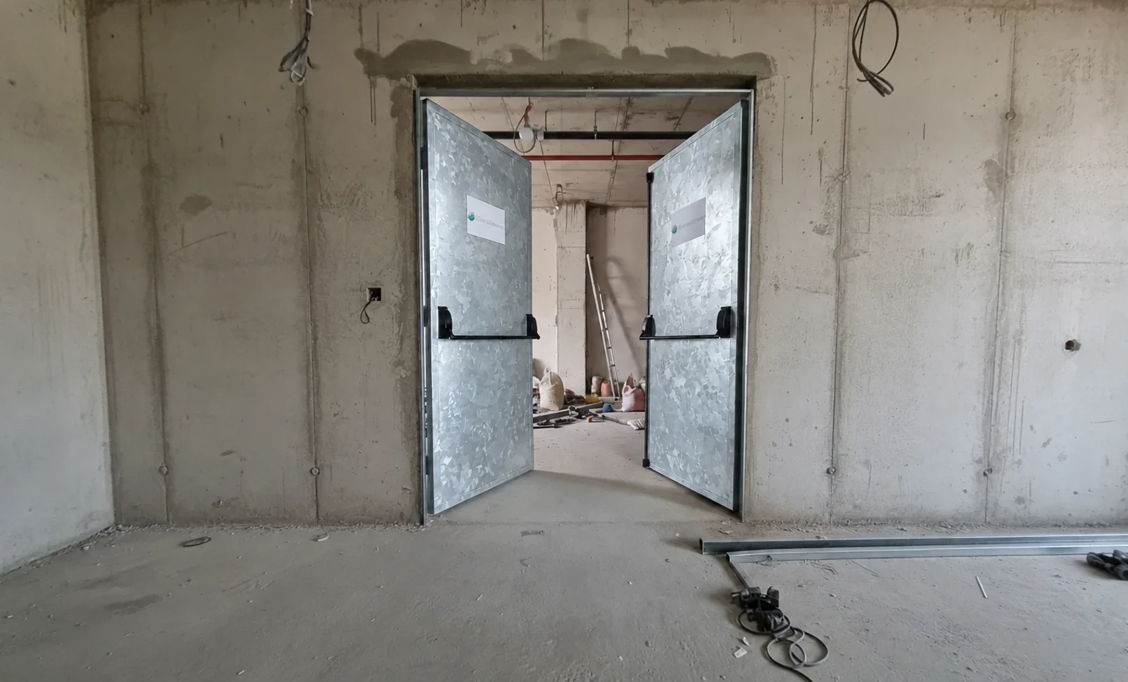 Porta de duas folhas abertas com acabamento com aspecto metálico e barras antipânico.